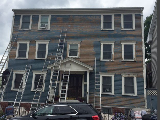 Three-family home before repainting, with staging up and old paint showing